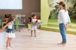 Professora conduz atividade sensorial com crianças em uma sala de aula, utilizando uma bola colorida para estimular movimento e interação